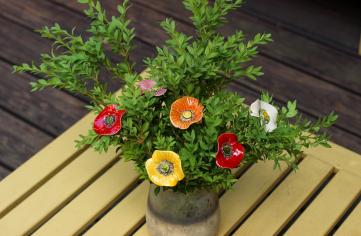 Mohnblumen aus Keramik zwischen lebenden Grünpflanzen