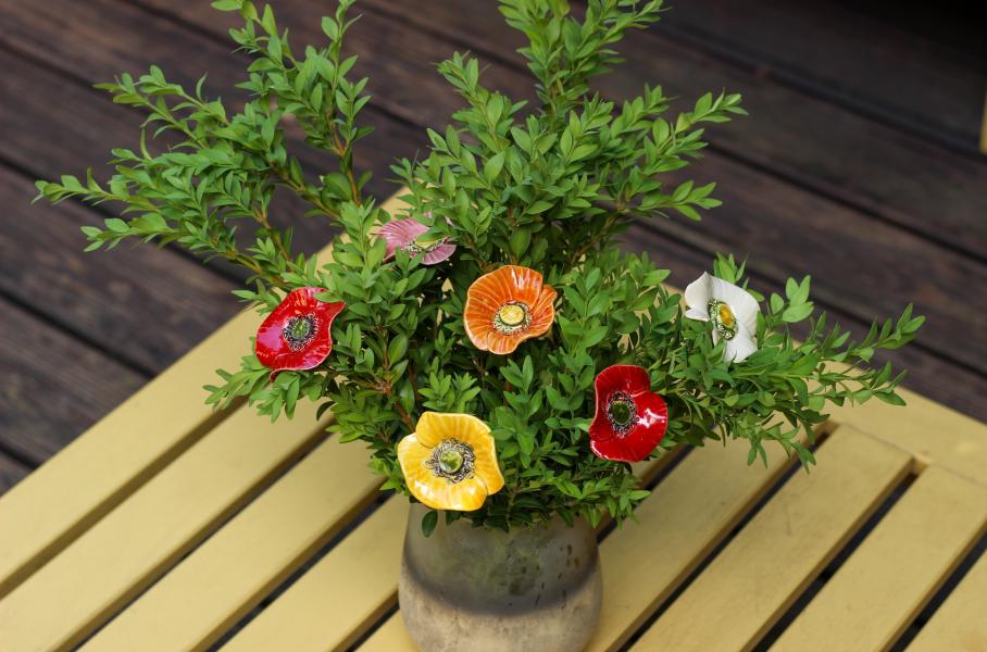 Mohnblumen aus Keramik zwischen lebenden Grünpflanzen